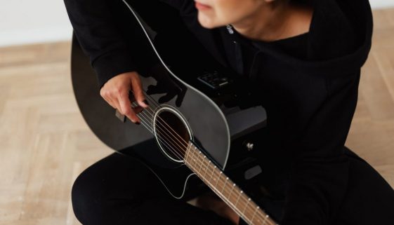 person in black long sleeve shirt playing acoustic guitar