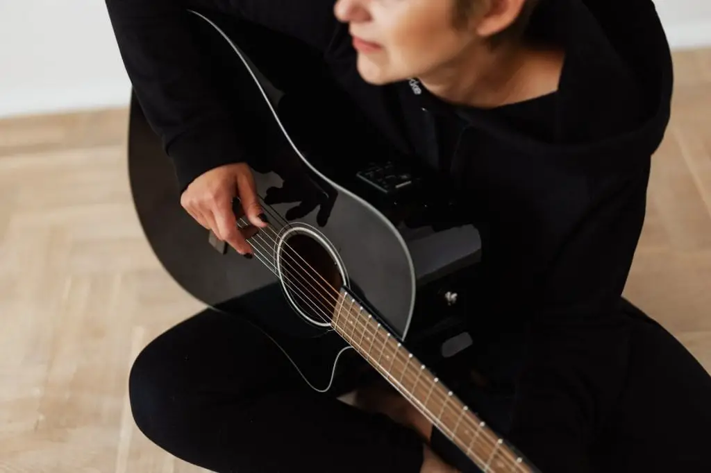 person in black long sleeve shirt playing acoustic guitar