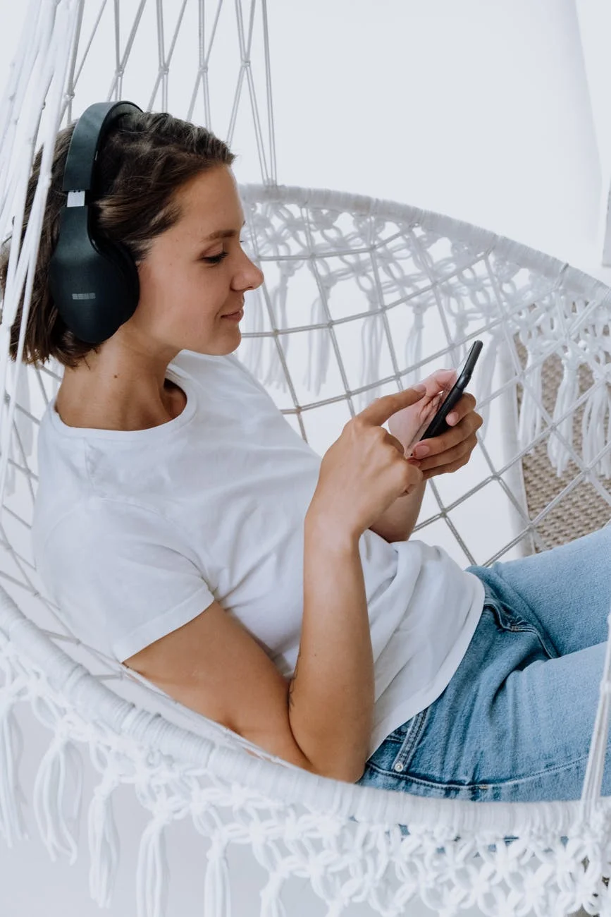 woman in white crew neck t shirt and blue denim jeans holding smartphone